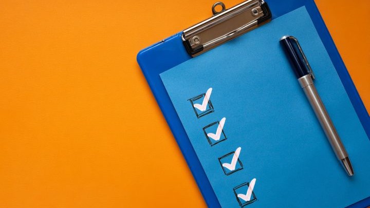 blue clipboard with four checkmarks and a pen on an orange background