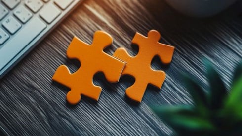 two orange puzzle pieces on a desk next to a keyboard and a plant