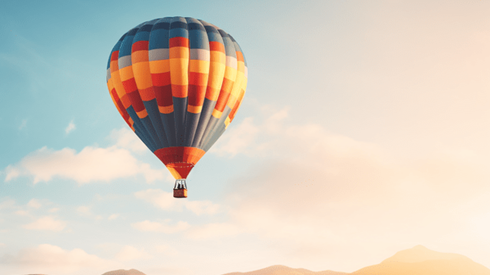 Colorful Hot Air Balloon Floats Above Mountaintops Against a Muted Partly Cloudy Sky