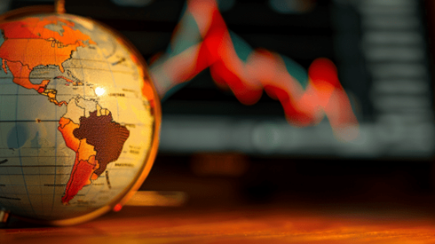 A globe on the left side of a desk with a computer screen showing a downward trending line graph in the background