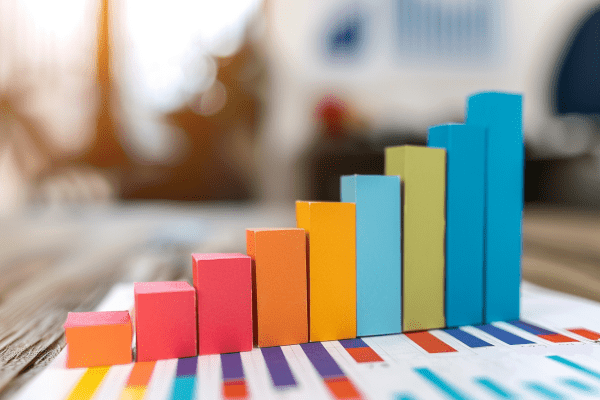 Multicolored upward rising bar graph made of construction paper and sitting on top of a sheet of paper with a bar graph drawn on it