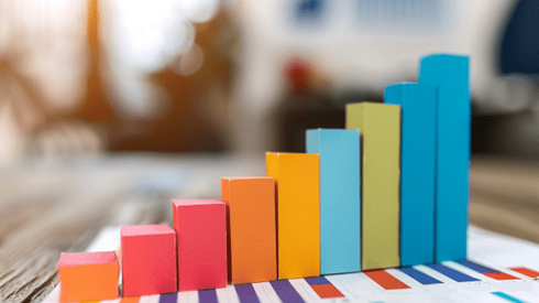 Multicolored upward rising bar graph made of construction paper and sitting on top of a sheet of paper with a bar graph drawn on it