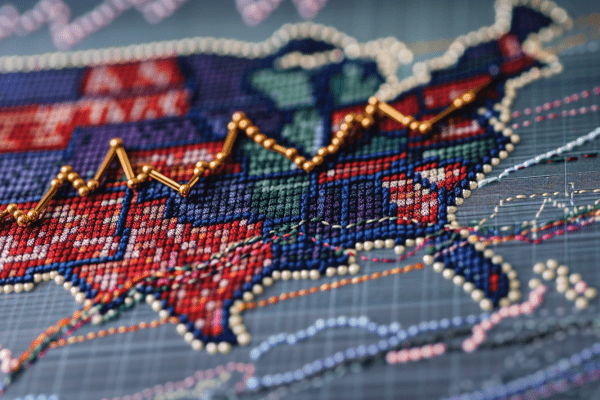 Cross-stitch map of United States with gold pinheads forming an upward-trending line graph
