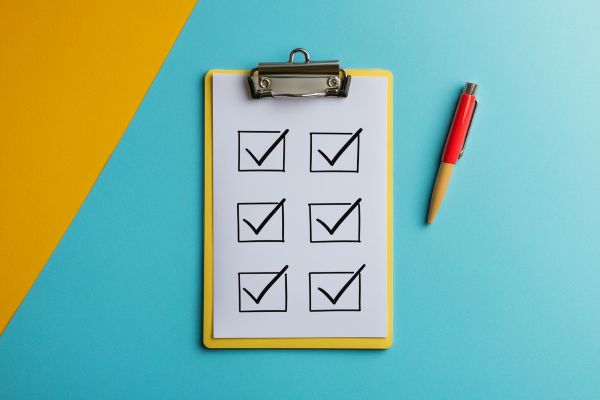 yellow clipboard with six boxes checked off next to a pen on a blue background