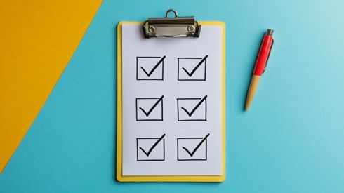 yellow clipboard with six boxes checked off next to a pen on a blue background