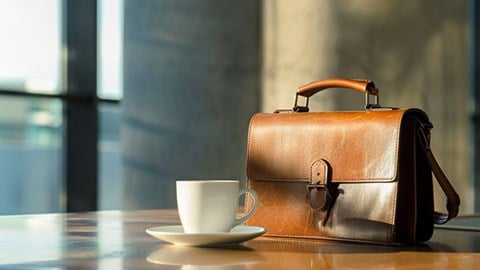 A leather briefcase resting on a table next to a white coffee mug.