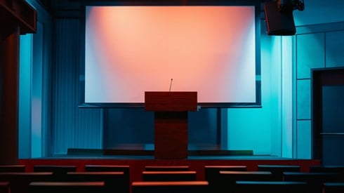An empty conference room with a podium and a blank projector screen behind it.