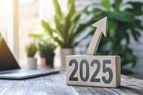 The number "2025" with an arrow sticking out of it and pointing upward siting on top of a desk next to a laptop.