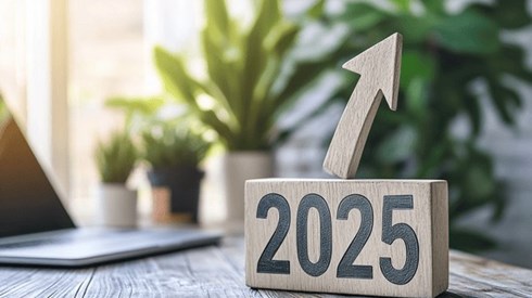 The number "2025" with an arrow sticking out of it and pointing upward siting on top of a desk next to a laptop.