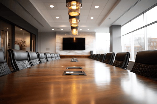 A boardroom with a large wooden conference table surrounded by black leather chairs