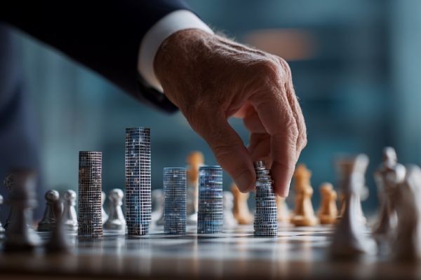 businessman's hand moving a chess piece shaped like a commerical building on a chess board