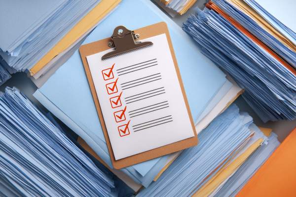 clipboard with five checked boxes on top of piles of papers