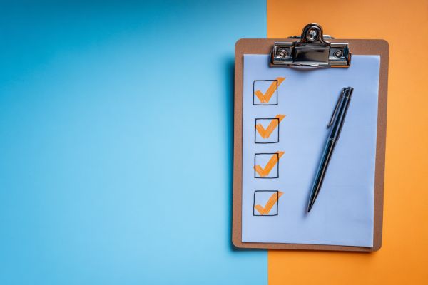 clipboard holding paper with four checked checkboxes and a pen resting on top on a blue and orange background