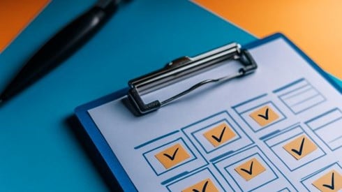 clipboard with orange boxes checked off next to a black pen