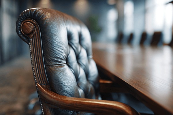 Close-up of a brown leather high-backed chair that is around a dark wooden conference table