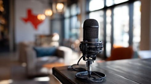 black podcast microphone on a table in a lobby with the outline of the state of Texas on the wall in the background