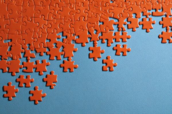 oddly shaped orange puzzle pieces connected into a partially completed puzzle on a blue table