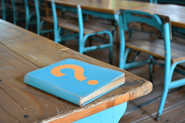Children's primer with an orange question mark on its front cover sitiing on an old school desk