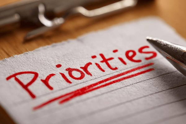 The word “Priorities” written in red ink and underlined on a piece of paper next to a pen