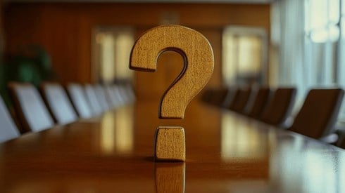 A wooden question mark sitiing on top of a conference table that is surrounded by chairs