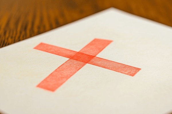 A red "X" on top of an off-white piece of paper on a wooden desk