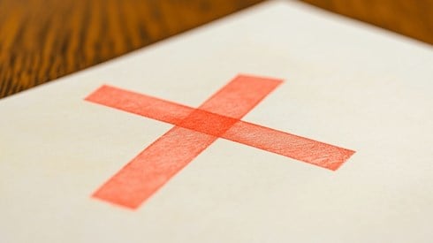 A red "X" on top of an off-white piece of paper on a wooden desk