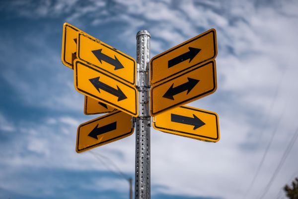 intentially confusing street sign pole with multiple orange signs with black arrows pointing in different directions