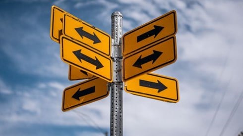intentially confusing street sign pole with multiple orange signs with black arrows pointing in different directions