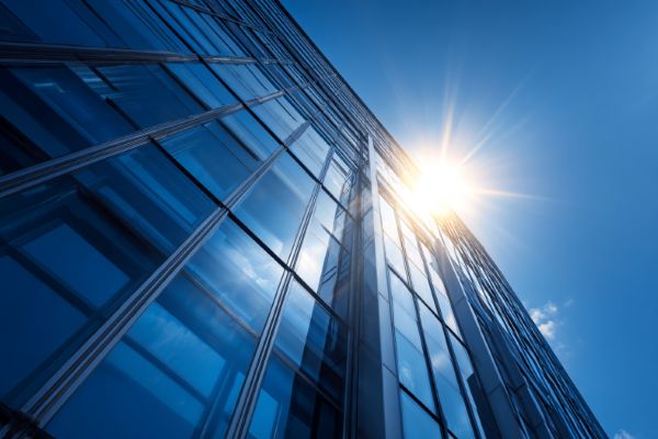 looking up from the ground at the sun coming up over a tall blue glass corporate building