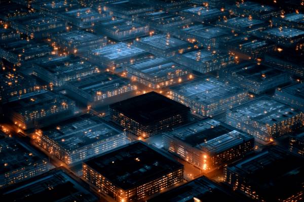 overhead view of a grid of data buildings, all lit in blue and orange lights except for one dark building in the middle