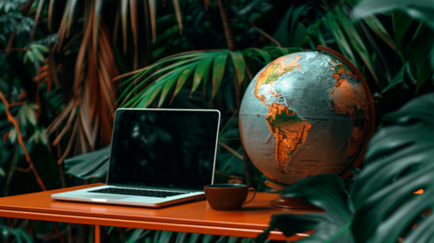 Laptop, coffee cup, and globe sitting on a desk in the jungle