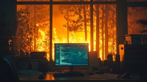 glowing computer monitor in front of a window showing a wildfire