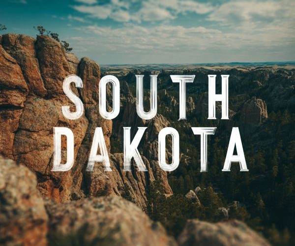 the words "SOUTH DAKOTA" superimposed over a landscape view of mountains and trees on a semi-cloudy day