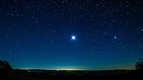 A single bright star shining in a clear night sky above the horizon.