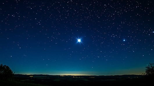 A single bright star shining in a clear night sky above the horizon.