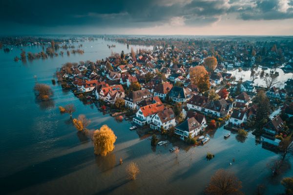 overhead view of a flooded residential area and houses next to a river with storm clouds in the background