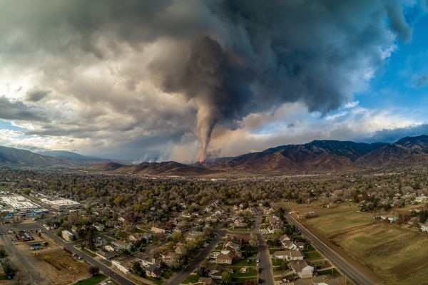 large tornado over a wildfire on a mountain near a town