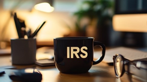 A black coffee mug with the letters "IRS" on it sitting on top of an office desk