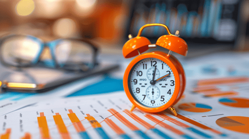 Orange alarm clock sitting on top of charts and graphs