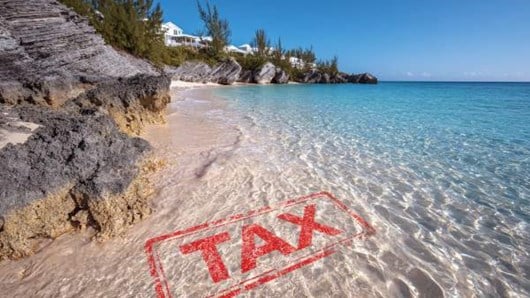 beach with sand and a house in the distance, red tax stamp superimposed under the water