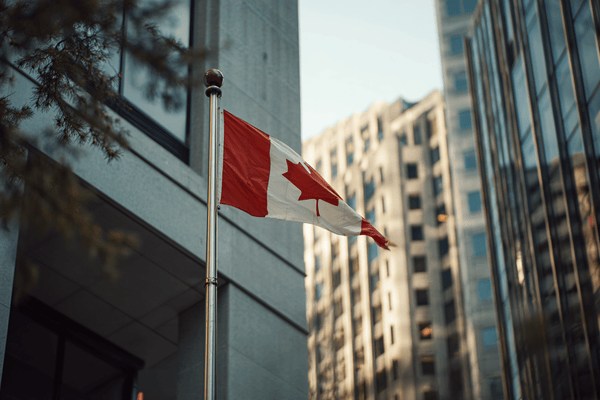 A Canadian flag waving in the wind on a flagpole in front of an office building
