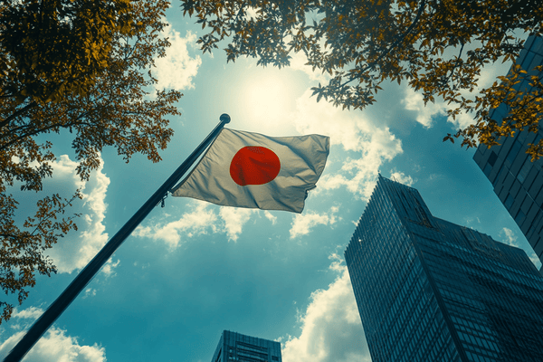 A Japanese flag flying from a flagpole below skyscrapers on a sunny day