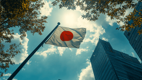 A Japanese flag flying from a flagpole below skyscrapers on a sunny day