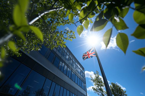 The UK flag on a flagpole in front of an office buiding on a sunny day