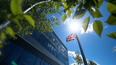 The UK flag on a flagpole in front of an office buiding on a sunny day