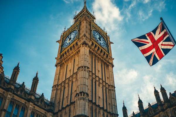 UK parliament building clock tower next to the UK flag flying on a pole
