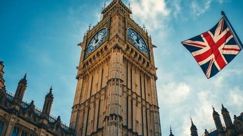 UK parliament building clock tower next to the UK flag flying on a pole