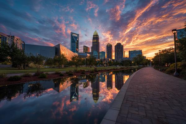Charlotte, North Carolina skyline behind a river with the sun and clouds in the background