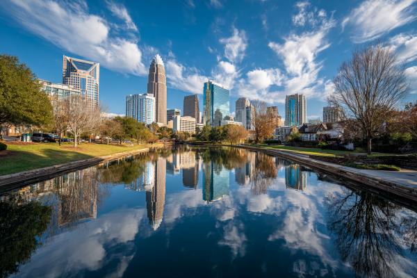 skyline of Charlotte, NC reflected in water with bright blue sky and clouds