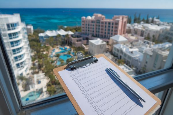 clipboard with paper with checkboxes and checks and a pen overlooking a window to Bermuda hotels and ocean